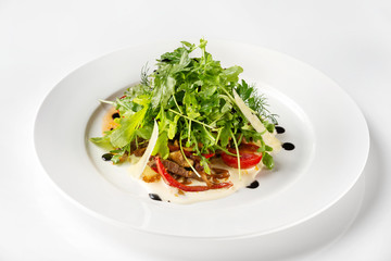 Plate of beef salad served with parmesan, green and tomato isolated at white background.