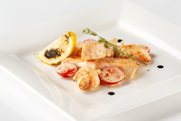 Plate with salmon fish steak served with prawns, lemon, tomato and sauce isolated at white background.