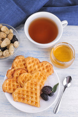 Delicious sweet Belgian waffles in the form of hearts with honey and tea on a blue wooden table. breakfast. top view