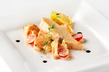 Plate with salmon fish steak served with prawns, lemon, tomato and sauce isolated at white background.