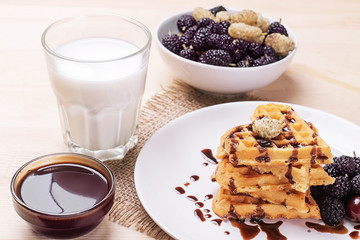 Delicious sweet Belgian waffles in the form of hearts with chocolate and berries with a glass of milk. breakfast. on a natural wooden background