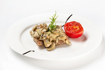 Plate of beef steak served with white mushrooms sauce and tomato isolated at white background.