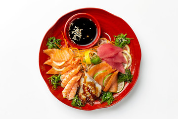 Top view isolated plate of sashimi including tuna, shrims, salmon served with soy sauce isolated at white background.