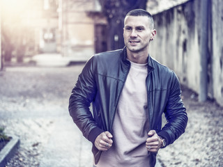 One handsome young man in urban setting in European city, standing, wearing black leather jacket and jeans