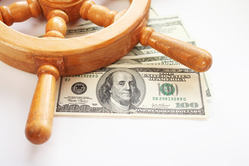 Wooden steering wheel on a ship and dollars on a white background