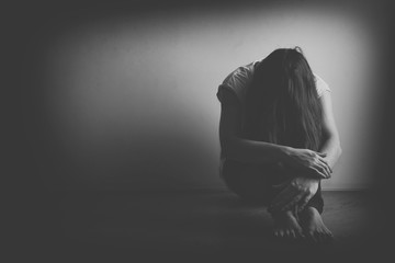 Teenager girl with depression sitting alone on the floor in the dark room. Black and white photo - obrazy, fototapety, plakaty