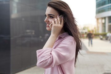 Fototapeta premium Busy female manager calling with cell telephone outside, woman talking via mobile phone and walking on the city street, manager working remotely and making phone call via modern smartphone outdoors