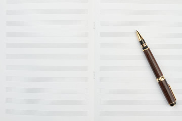 Pen on musical notes and copy space. Top view on blank notebook for musical notes and ballpoint pen, vertical image. Musical education accessories.