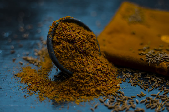 Close up of powdered cumin or zeera or jeera with raw cumin on wooden surface in a clay bowl on a cloth or napkin.