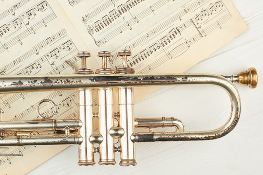Old rusty trumpet and musical notes. Close up vintage trumpet and musical sheets on light background, horizontal image.