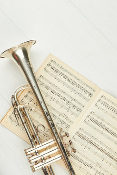 Rusty trumpet on musical notes, top view. Music notes book and trumpet with clipping path. Classical wind instrument.