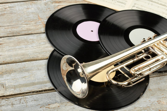 Retro musical objects close up. Wooden background with vinyl records, trumpet and music sheets. Vintage musical objects.