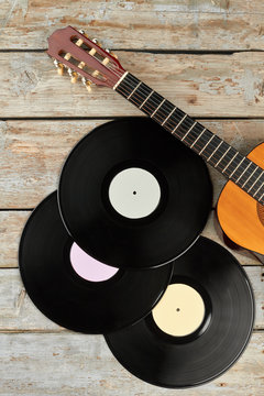 Vinyl records and wooden guitar. Three vinyl plates and guitar on wooden background, top view. Vintage musical equipment.