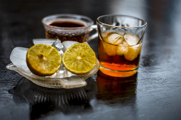 Close up of hangover remedy i.e. lemon juice and black tea in a transparent cup on wooden surface with Scotch or Scotch whiskey or Grain whiskey.