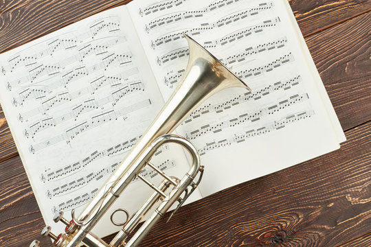 Trumpet on musical notes book. Pipe and musical notes on wooden background. Music still life.
