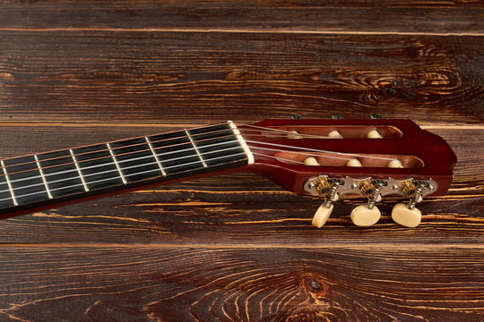 Fretboard of guitar on wooden background. Head of acoustic guitar on brown wooden surface. Classical music instrument.