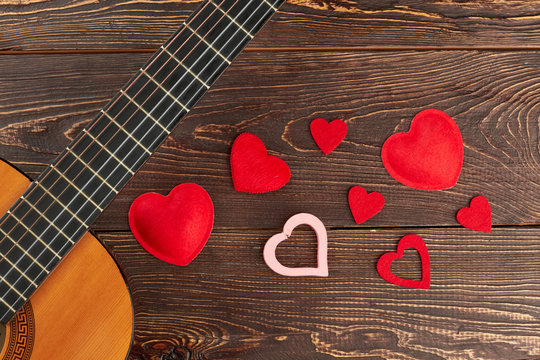 Guitar and red hearts on wooden background. Ukulele guitar and heart-shaped decorations. Valentines Day background.