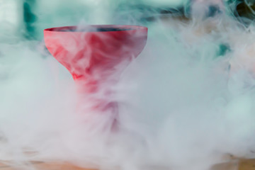 Fototapeta premium red bowl of the hookah sitting on the table, shrouded in smoke
