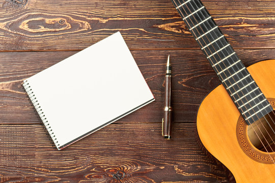 Guitar with blank notebook and pen. Workspace with blank notebook, pen and acoustic guitar on brown wooden table background. Work space of songwriter.