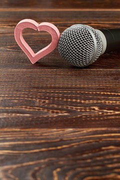 Microphone and pink heart on wooden background. Microphone and heart shaped decoration, copy space. Music of love.