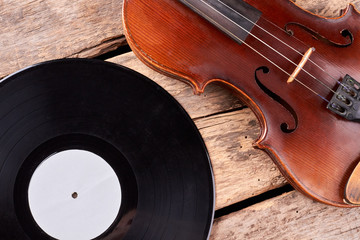 Musical background in retro style. Close up vintage violin and vinyl record on old wooden planks.