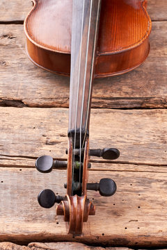Old violin part on wooden planks close up. Scroll and peg box of violin instrument. Details of design. Stringed musical instrument in vintage style.
