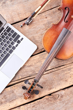 Vintage violin and laptop on wooden boards. Silver laptop and retro violin on rustic wooden planks. Old and modern technology concept.