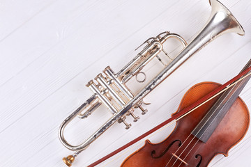 Obraz premium Instruments of orchestra and copy space. Old rusty trumpet, violin and fiddle stick on white wooden surface.