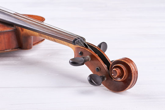 Violin scroll and peg box. Part of violin on white wooden background. Construction of old musical instrument.