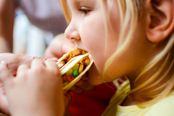 children, diet, culinary and food concept .Young blonde girl eating tortilla with meat and...