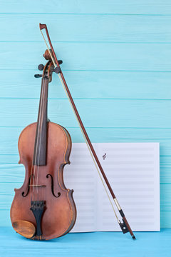 Classical music background. Violin, bow and musical notes papers on blue wooden background, vertical image.