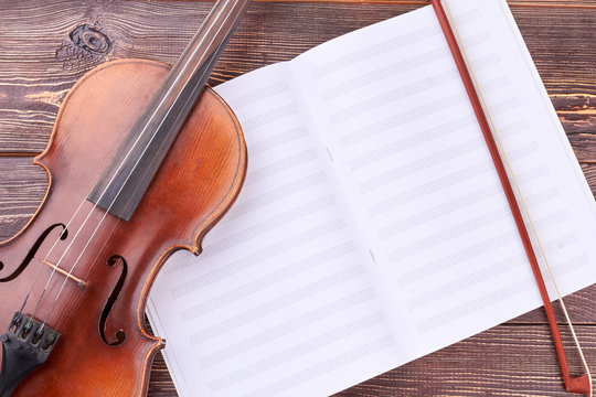 Violin, bow and musical notes. Brown violin and bow on musical sheets. Classical equipment of orchestra.