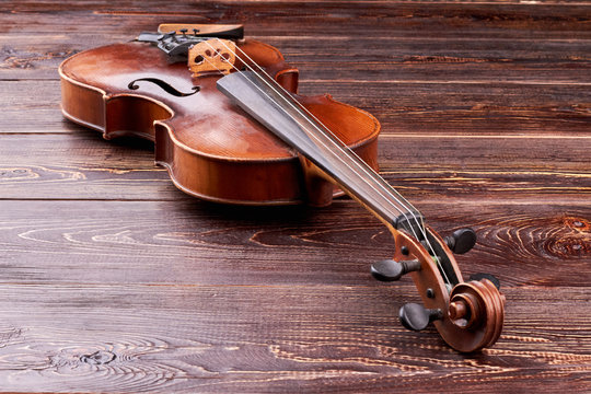 Violin on brown wooden background. Stringed musical instrument and copy space. Antique equipment of classical music.