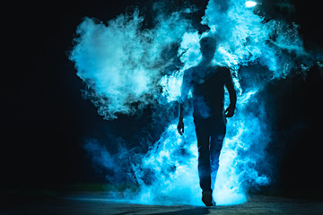 The man walking in the blue smoke on the dark background - Powered by Adobe