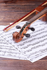 Naklejka premium Violin and musical notes on wooden background. Violin scroll and peg box on musical note sheets. Lesson of classical music.