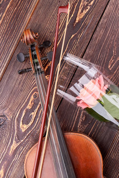Violin and pink rose on wooden background. Vintage violin, fiddle stick and delicate flower on brown textured wood. Music and nature.