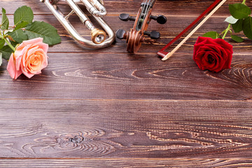 Musical instruments and roses on wooden background. Trumpet, violin, fiddle stick, roses and copy space. Music still life.