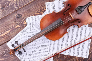 Old violin and musical notes. Vintage violin, bow and music sheets on brown wooden background. Classical stringed instrument.
