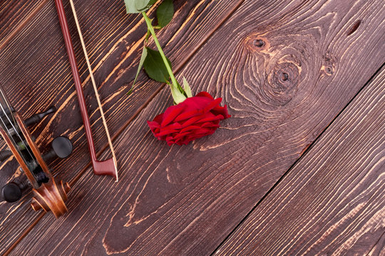 Violin, bow, rose and copy space. Old violin, fiddle stick and red rose on textured wooden background with text space.