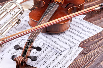 Close up violin, bow and musical notes. Vintage violin, trumpet and music sheets on wooden background. Classical music instruments background.