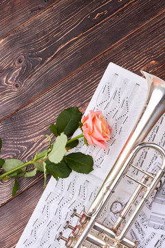 Trumpet, musical notes and pink rose. Musical notes sheets with trumpet and rose flower on dark wooden background, top view. Romantic music background.