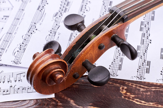 Old violin scroll and peg box. The head of intage violin on music notes background. Construction of antique violin instrument.