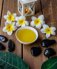 Fototapeta na wymiar massage oil with plumeria flowers, black round stones and orange candle on wooden surface