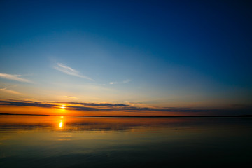 Fototapeta na wymiar Bright sun rolling down the horizon line. Blue sky over local lake