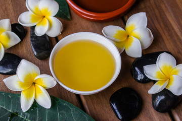 Fototapeta na wymiar massage oil with plumeria flowers, black round stones and orange candle on wooden surface