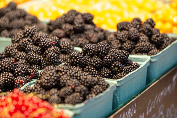 Closeup of a cardboard full of fresh organic blackberries and fruits at a pubic market