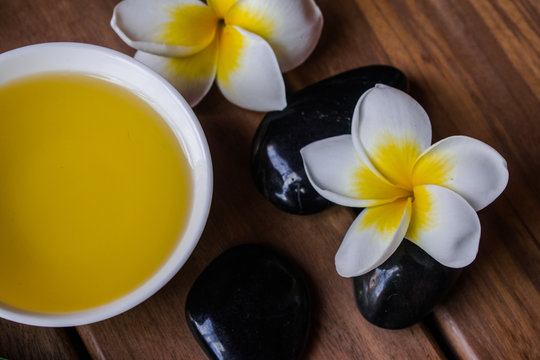 massage oil with plumeria flowers, black round stones  on wooden surface