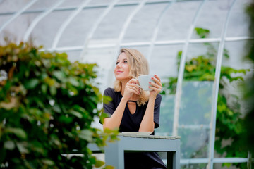 Young style girl with cup of coffee in a green autumn season garden in Belgium.