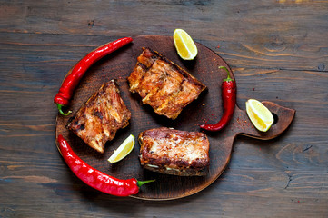 Spicy hot grilled spare ribs from BBQ served with  hot chili pepper and lime on dark wooden background.  Banner.  Top view,  copy space, flat lay.