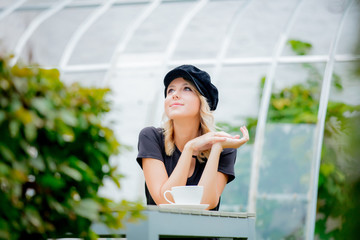 Young style girl in black dress and hat with cup of coffee in a green autumn season garden in Belgium.